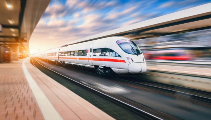 White modern speed train in motion on railway station at sunset. Train on railroad track with motion blur effect in Europe in evening. Railway platform. Industrial landscape. Railway tourism White modern speed train in motion on railway station at sunset. Train on railroad track with motion blur effect in Europe in evening. Railway platform. Industrial landscape. Railway tourism
